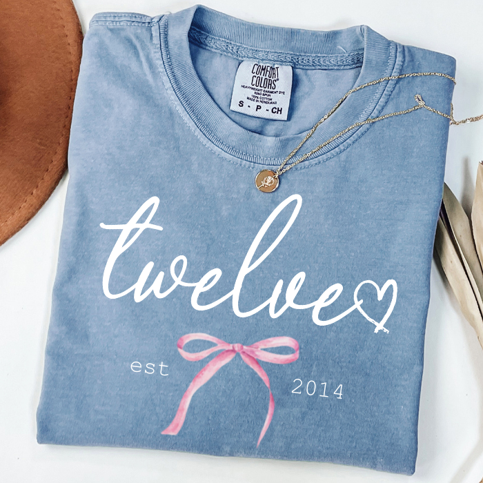 Light blue Comfort Colors 12th birthday shirt for girls featuring Twelve script, pink bow, and Est. 2014 design, boutique milestone birthday tee