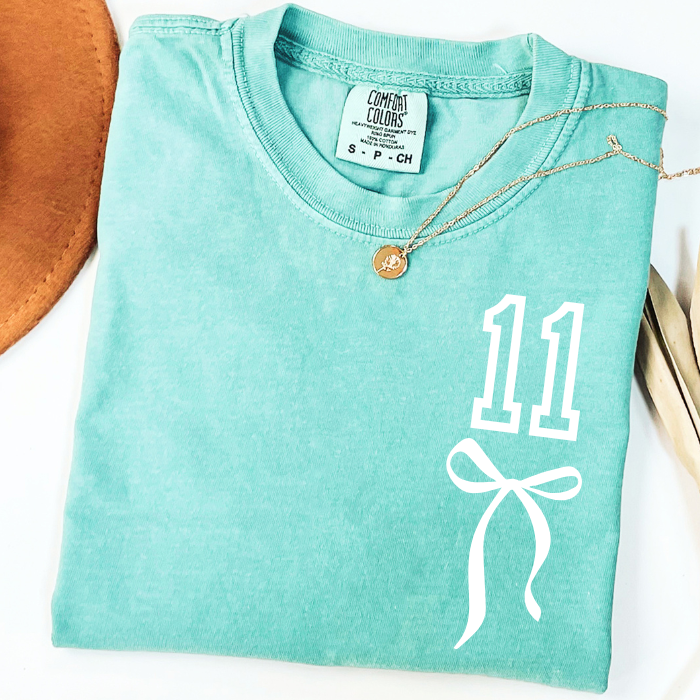 Mint green Comfort Colors 11th birthday shirt featuring white number 11 and coquette bow graphic