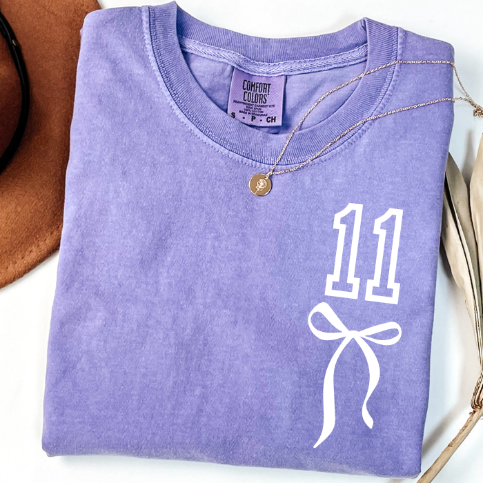 Lavender purple Comfort Colors 11th birthday shirt for girls featuring white number 11 with coquette bow design