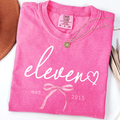 Pink Comfort Colors 11th birthday shirt for girls featuring elegant script eleven design with bow detail
