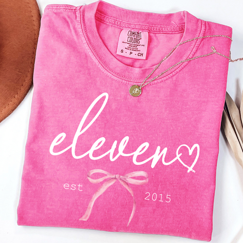 Pink Comfort Colors 11th birthday shirt for girls featuring elegant script eleven design with bow detail