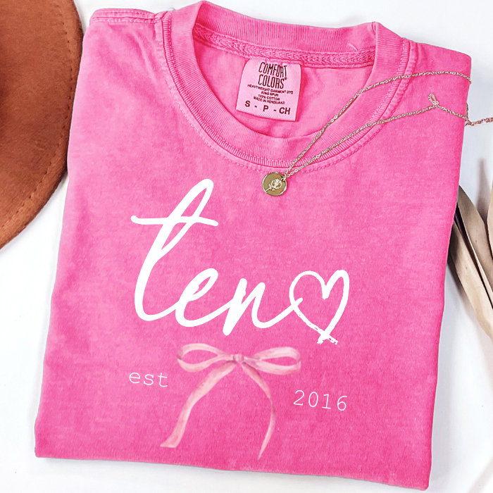 Pink Comfort Colors 10th birthday shirt for girls featuring elegant script eleven design with bow detail